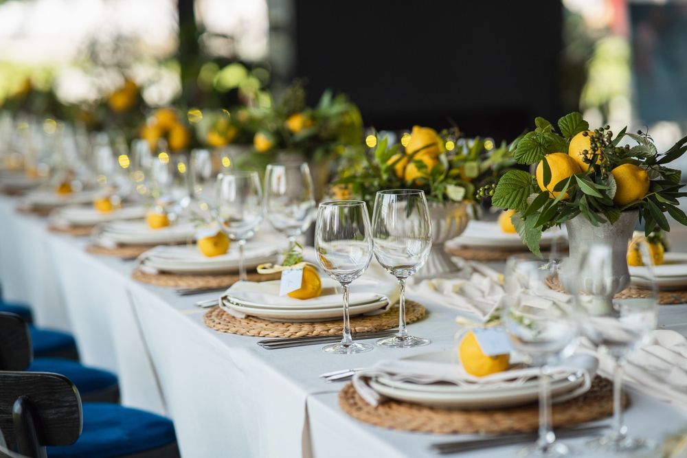 Elegant outdoor banquet table with white linens, yellow floral centerpieces, and neatly set glassware and plates
