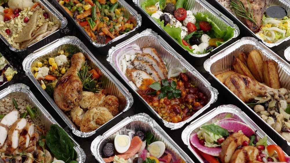 Assorted plated meals in takeaway containers, including meats, vegetables, and salads, arranged in rows.