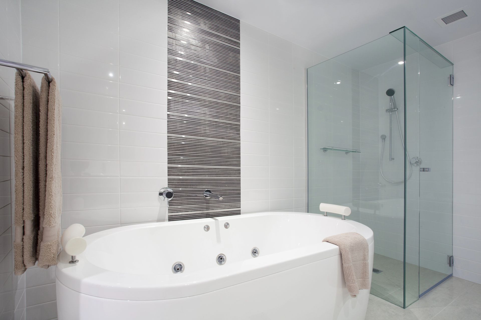 Un bagno moderno e bianco con vasca idromassaggio, una parete decorativa piastrellata e una doccia con box in vetro.