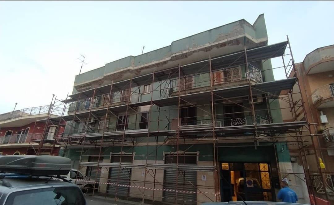 Un edificio verde a più piani in costruzione, ricoperto da impalcature metalliche, visto dal livello della strada.