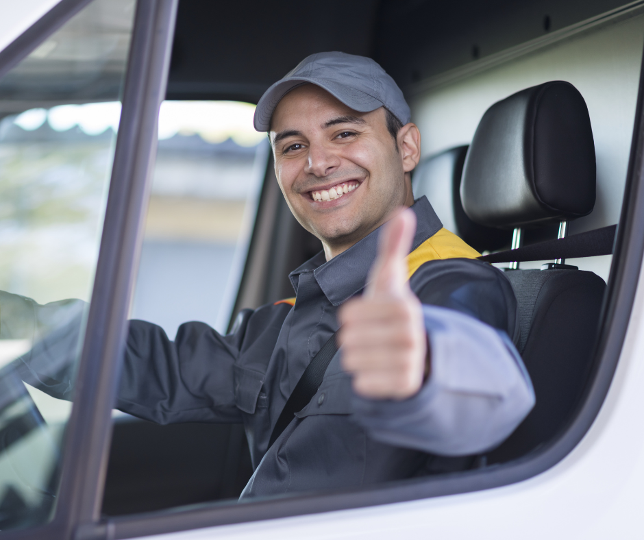 A delivery driver in a uniform and cap sits in a vehicle, smiling and giving a thumbs-up gesture.