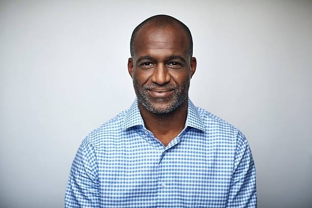 Man in blue and white checkered shirt smiles at camera against a white backdrop.