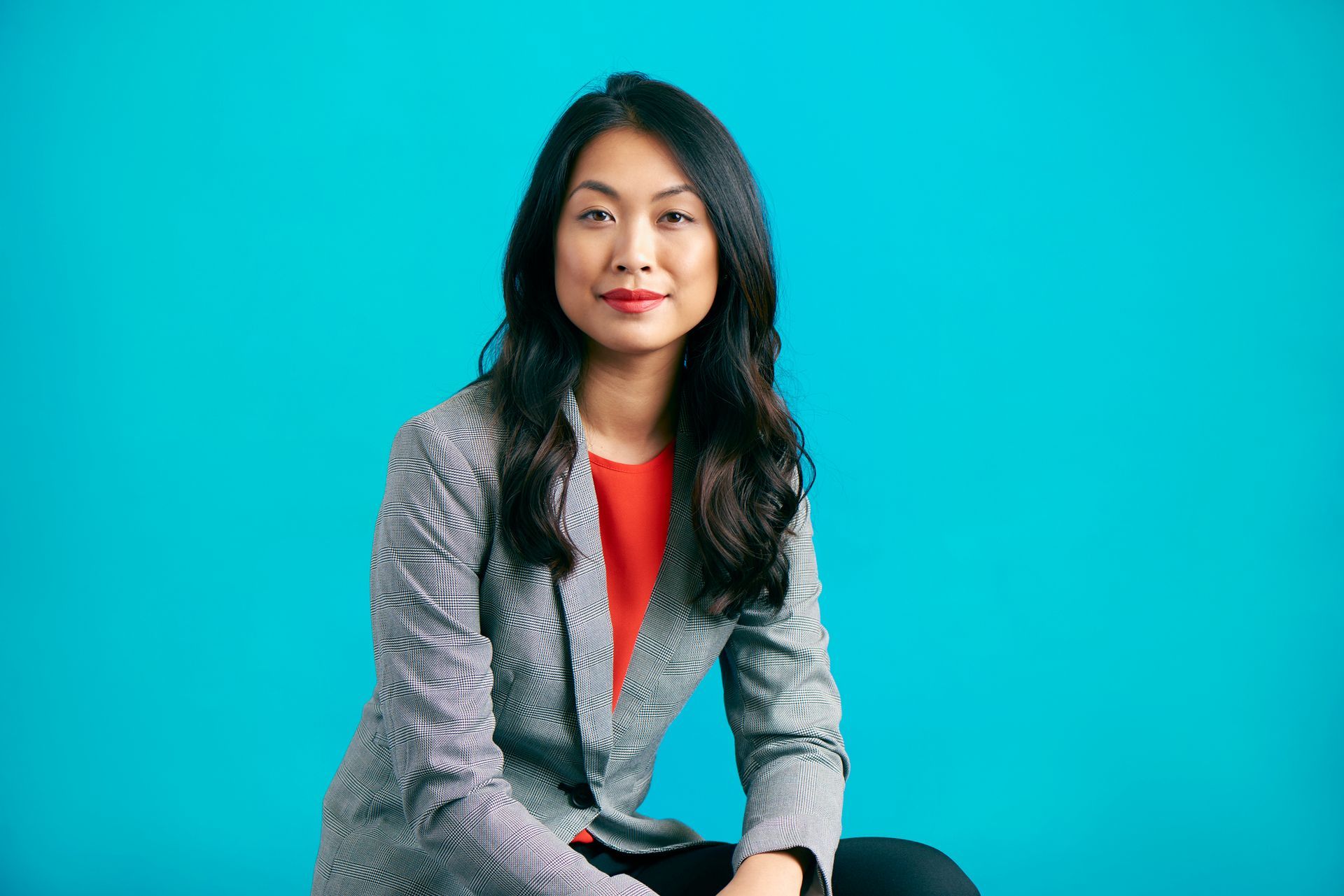 Woman in patterned blazer and red shirt against blue backdrop.