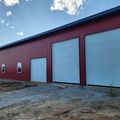 Red metal building with three white garage doors and two small windows.