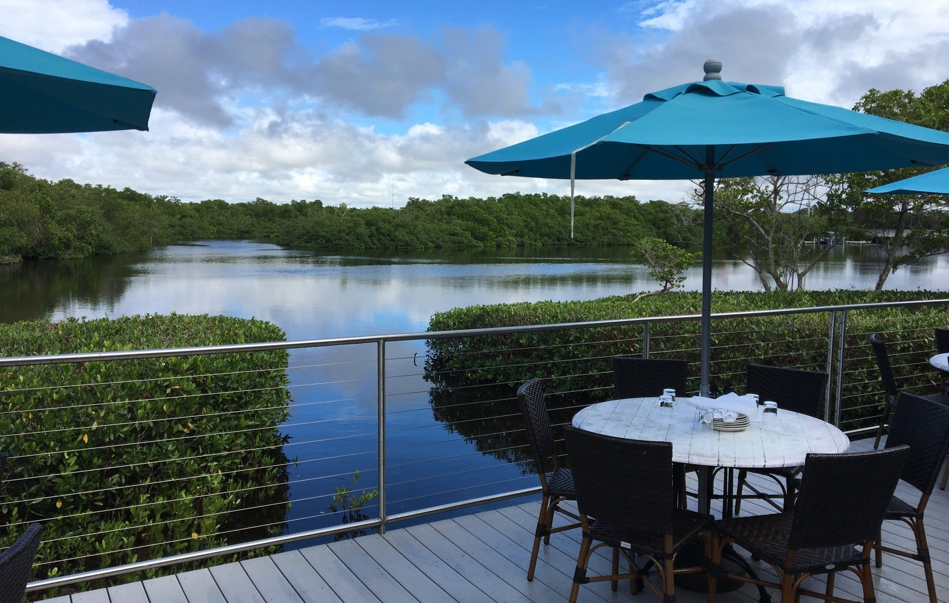 Patio overlooking a calm lake, with teal umbrellas and a table and chairs by the water.