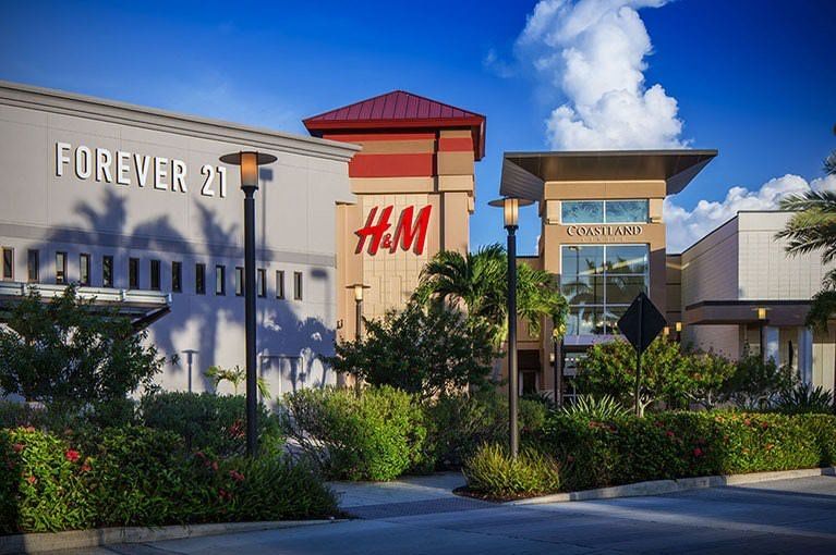 Shopping center with Forever 21 and H&M storefronts amid greenery at dusk