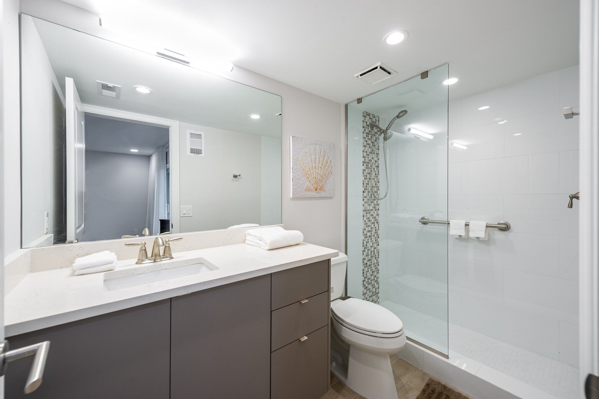 Modern bathroom with double vanity, large mirror, glass shower, and toilet