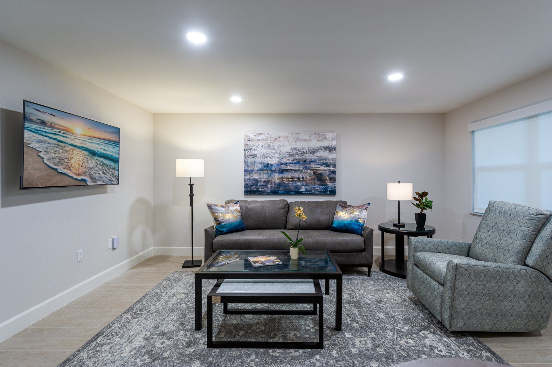 Modern living room with gray sofa, armchair, lamps, coffee table, and abstract wall art