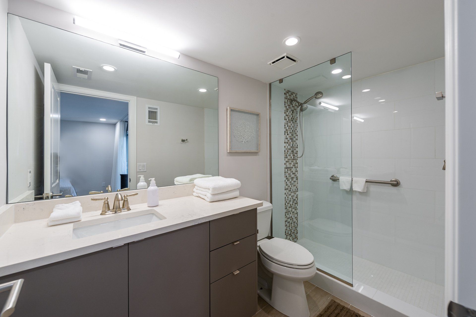 Modern bathroom with double vanity, large mirror, toilet, and glass-enclosed shower