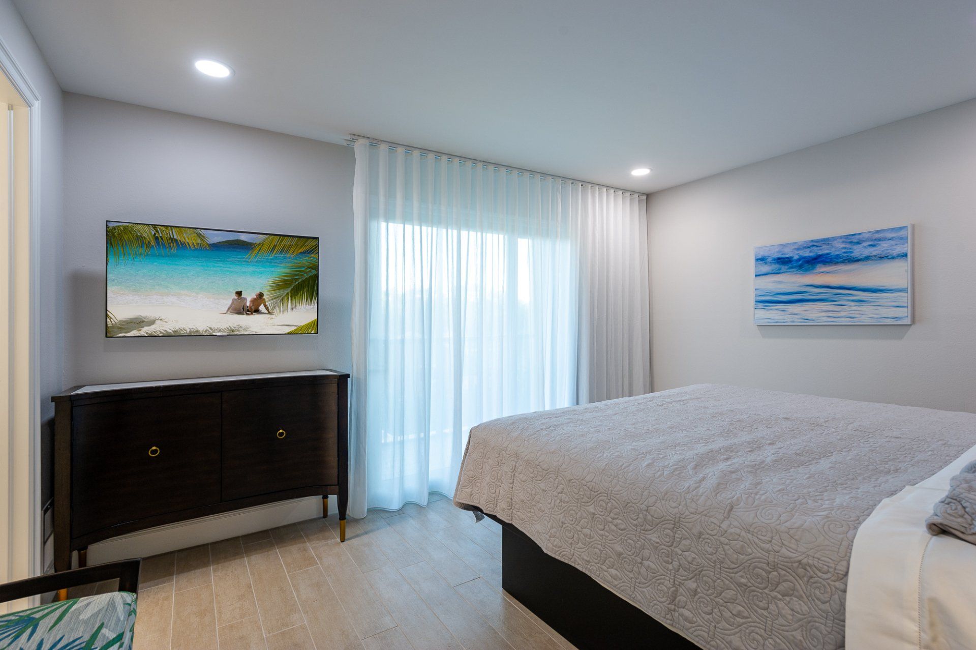Modern bedroom with bed, dresser, sliding glass doors, and beach-themed wall art