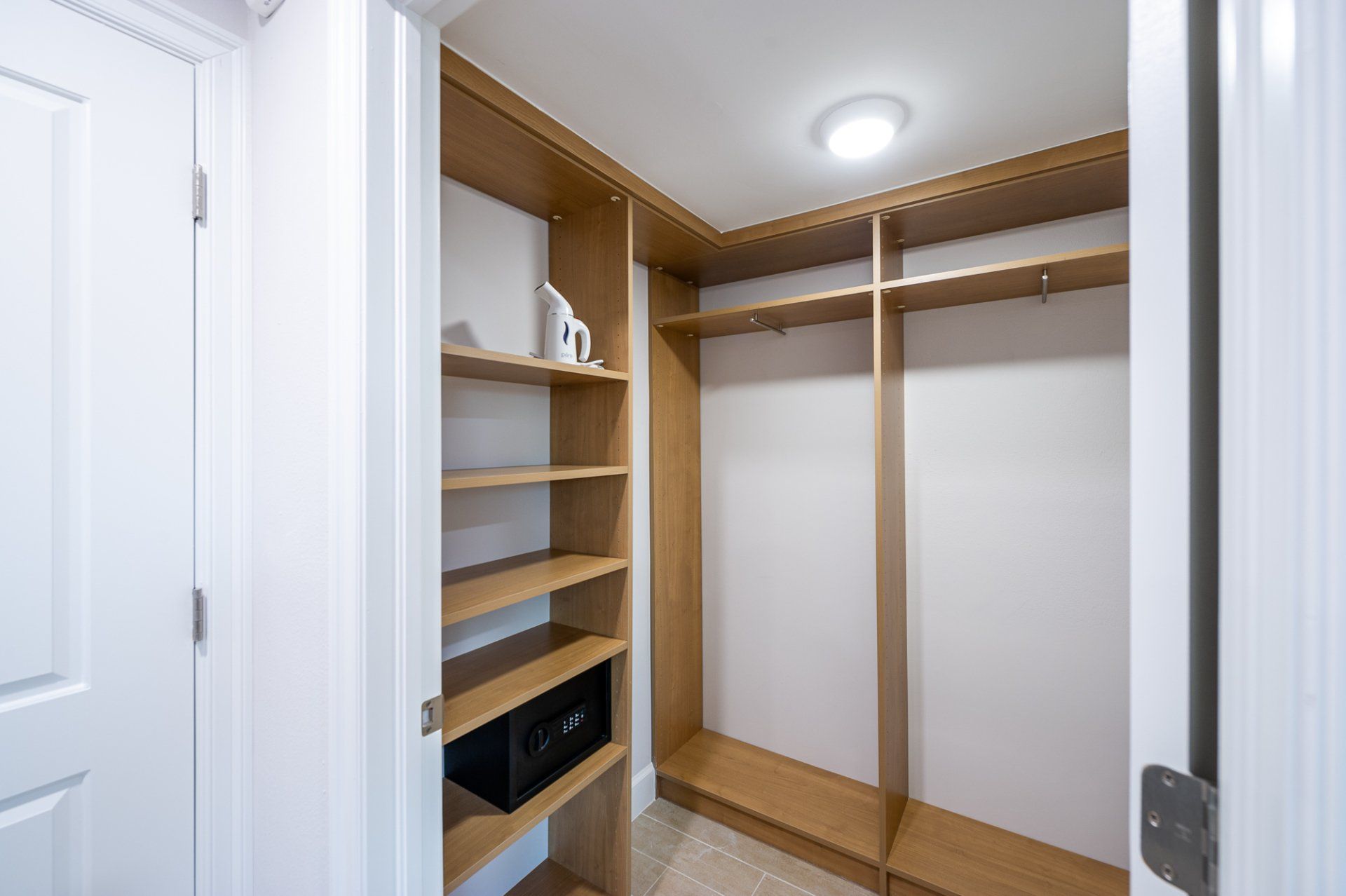 Empty walk-in closet with wooden shelves, hanging rods, and a ceiling light.