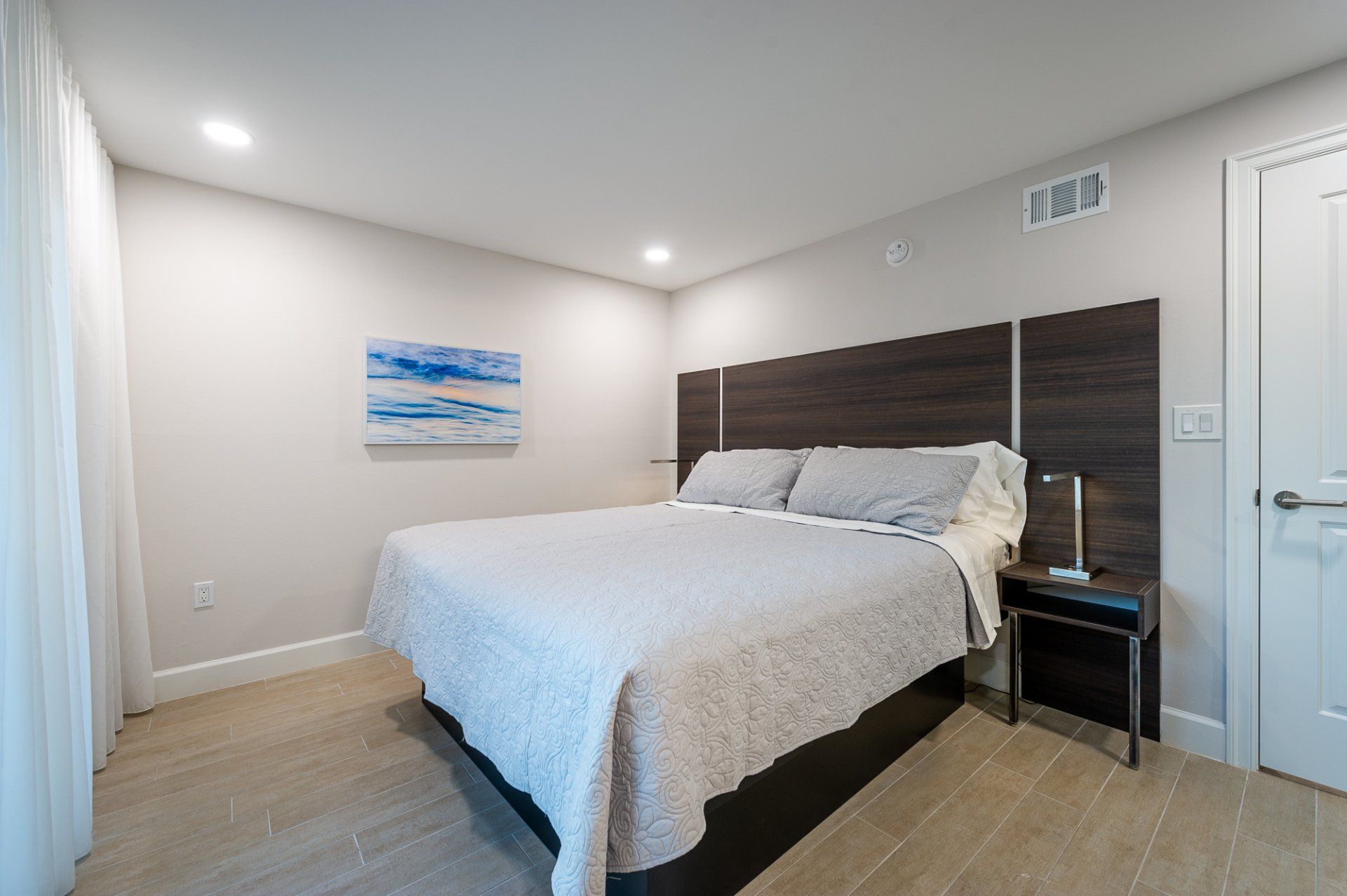 Modern bedroom with a bed, dark wood headboard, nightstand, and wall art in a bright neutral room