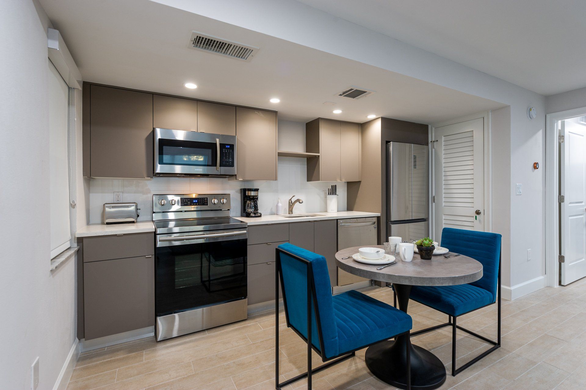 Modern kitchen with stainless steel appliances and a small round dining table with blue chairs