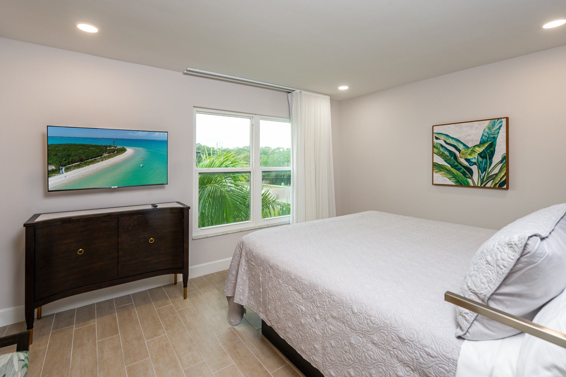 Bright bedroom with a bed, dresser, wall art, and a window overlooking greenery