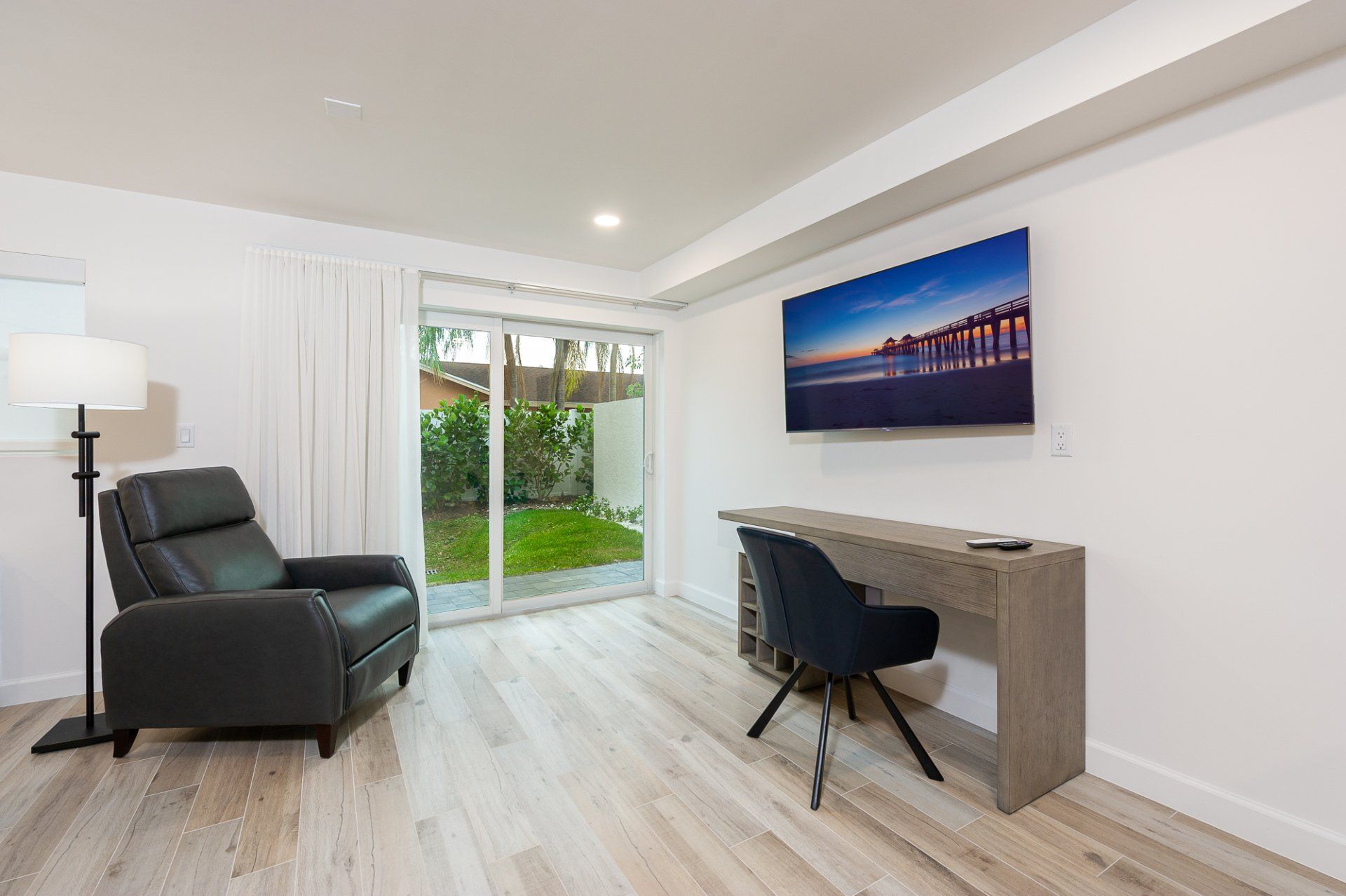 Modern living room with black chair, desk, wall-mounted TV, and sliding doors to a garden.
