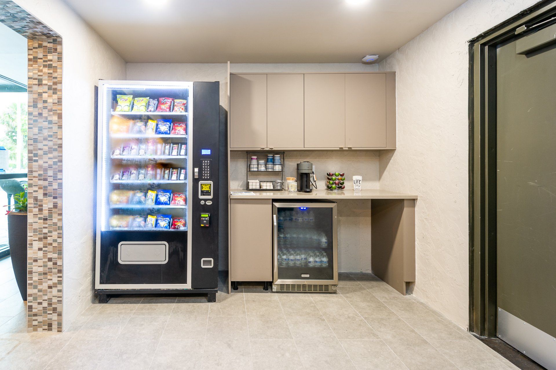 Small break room with vending machine, coffee station, and beige walls in a lobby area