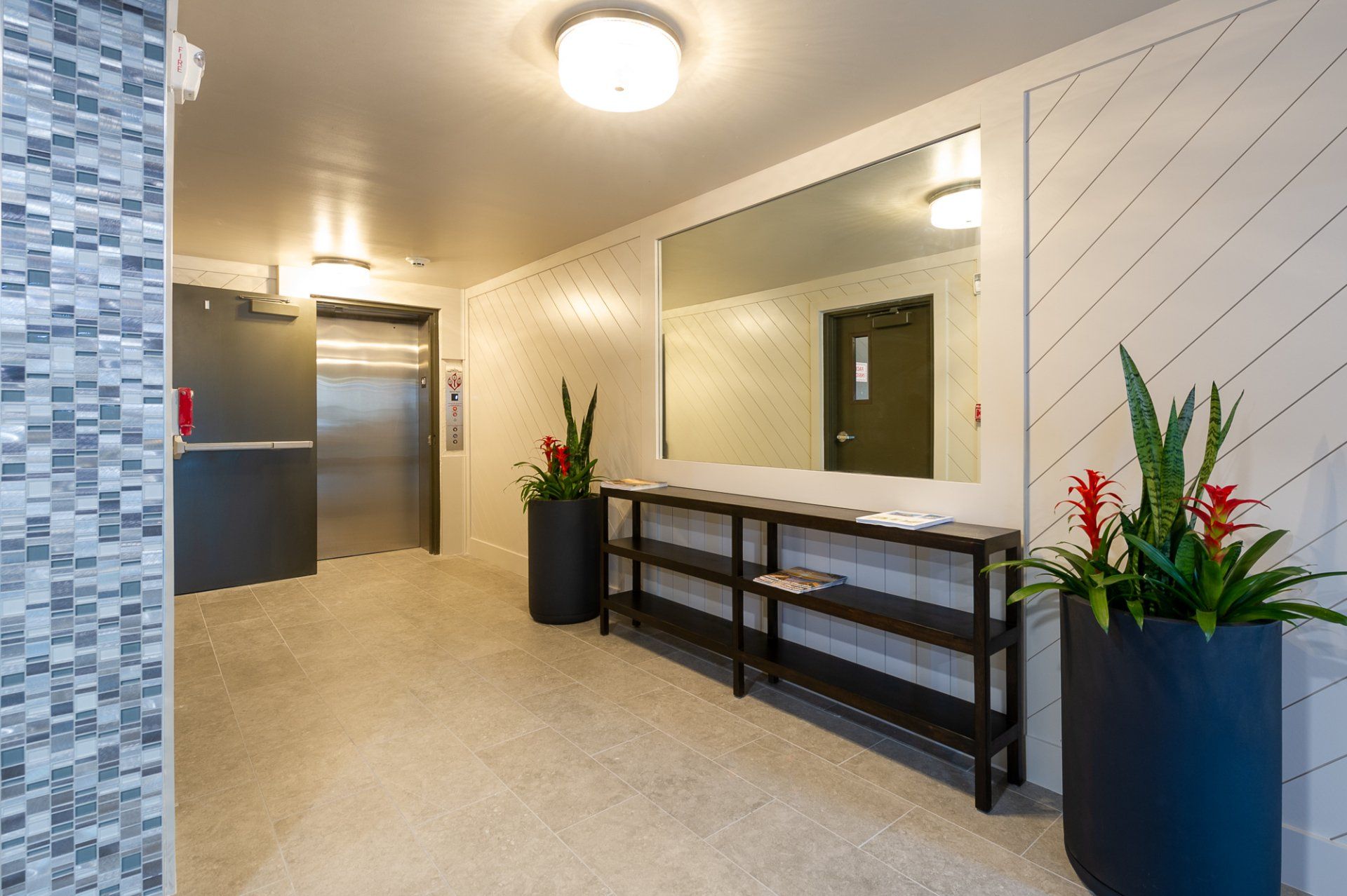 Modern apartment lobby with elevator, console table, mirror, and potted plants