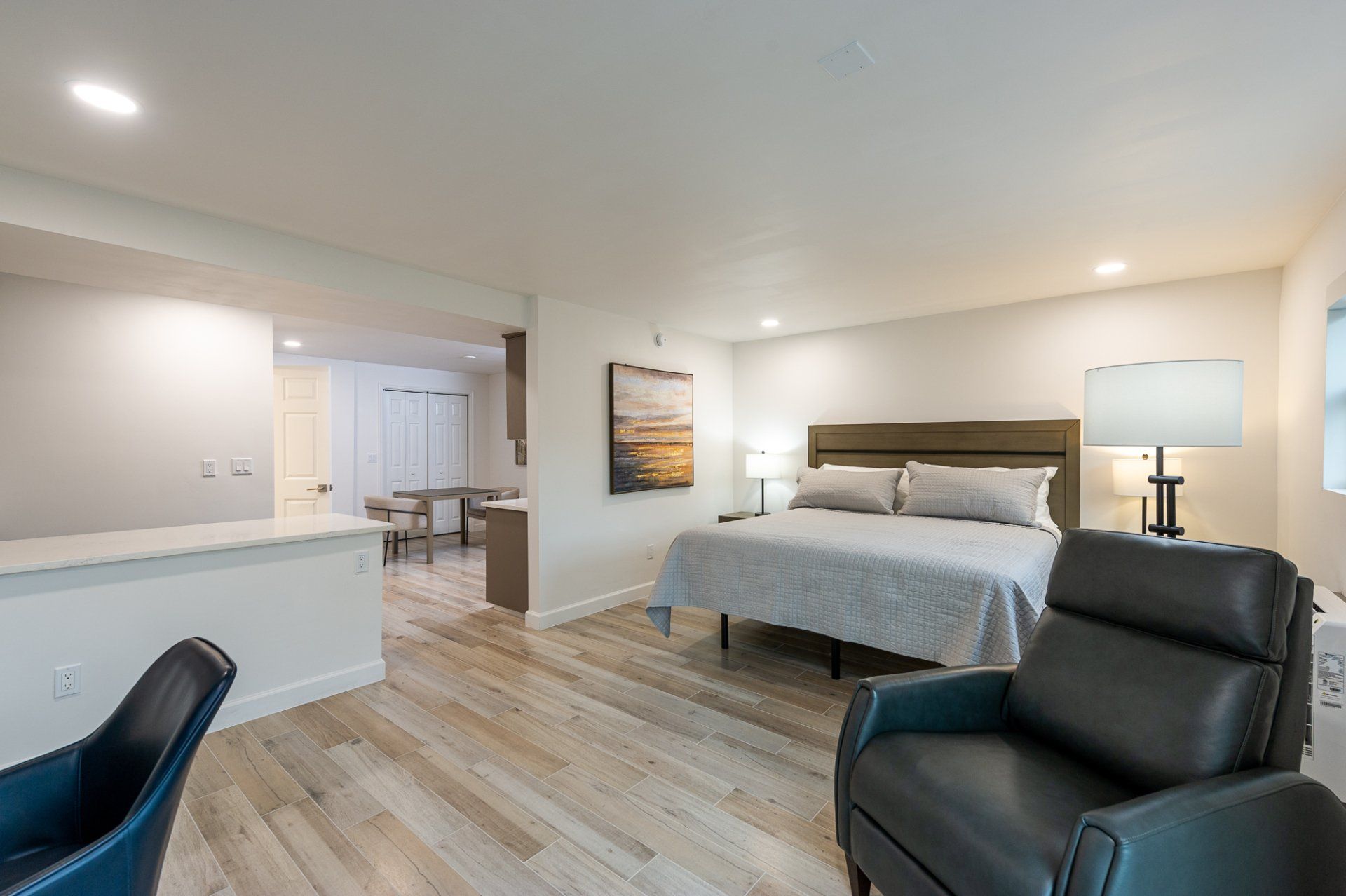 Spacious modern bedroom with a bed, two black chairs, and soft neutral decor