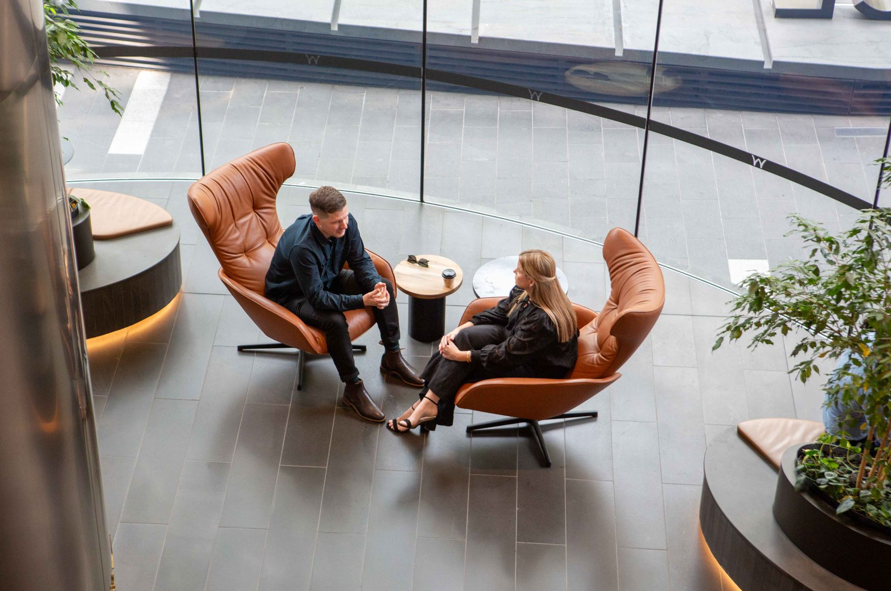 Two people in business attire sit on a gray sofa in a bright, modern waiting room.