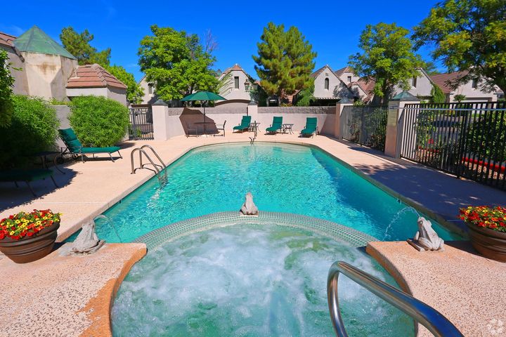 A large swimming pool is surrounded by chairs and umbrellas in a backyard.