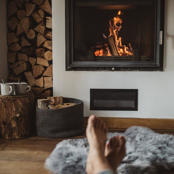 Cozy fireplace with burning fire, stacked logs, and feet resting on a rug in the foreground