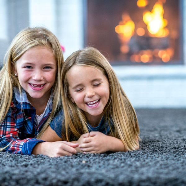 Two smiling children lying on a carpet near a lit fireplace