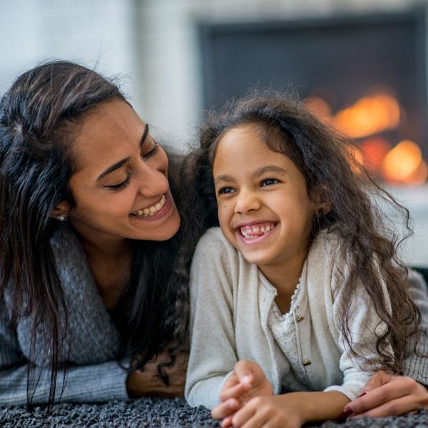 Two smiling people lying on a carpet by a glowing fireplace