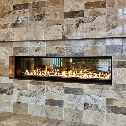 Modern linear gas fireplace set into a beige stone wall with visible flames.