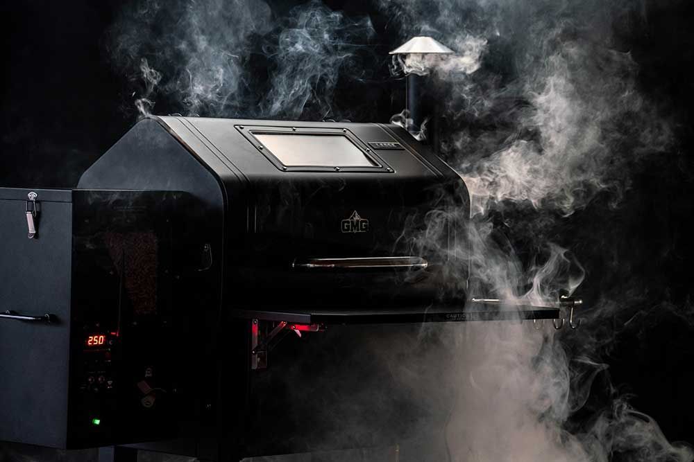 Smoke rising from a black outdoor smoker grill in a dark setting