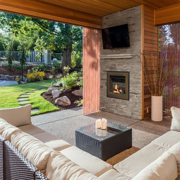 Cozy covered patio with sectional seating, fire pit, wall fireplace, and a view of a landscaped backyard