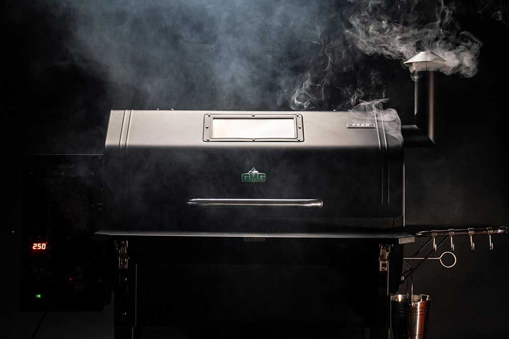 Black smoker grill with lid open, releasing steam and smoke in a dark setting.