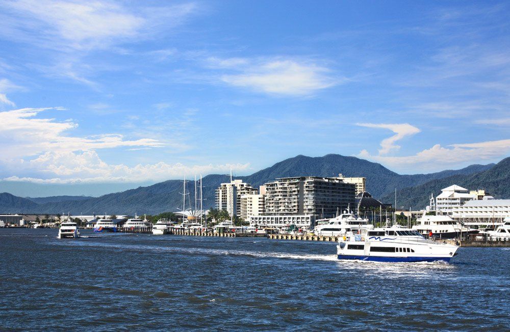 A Boat is Floating on Top of a Body of Water in Front of a City — SVS Auto Repairs & Dyno Tuning in Cairns, QLD