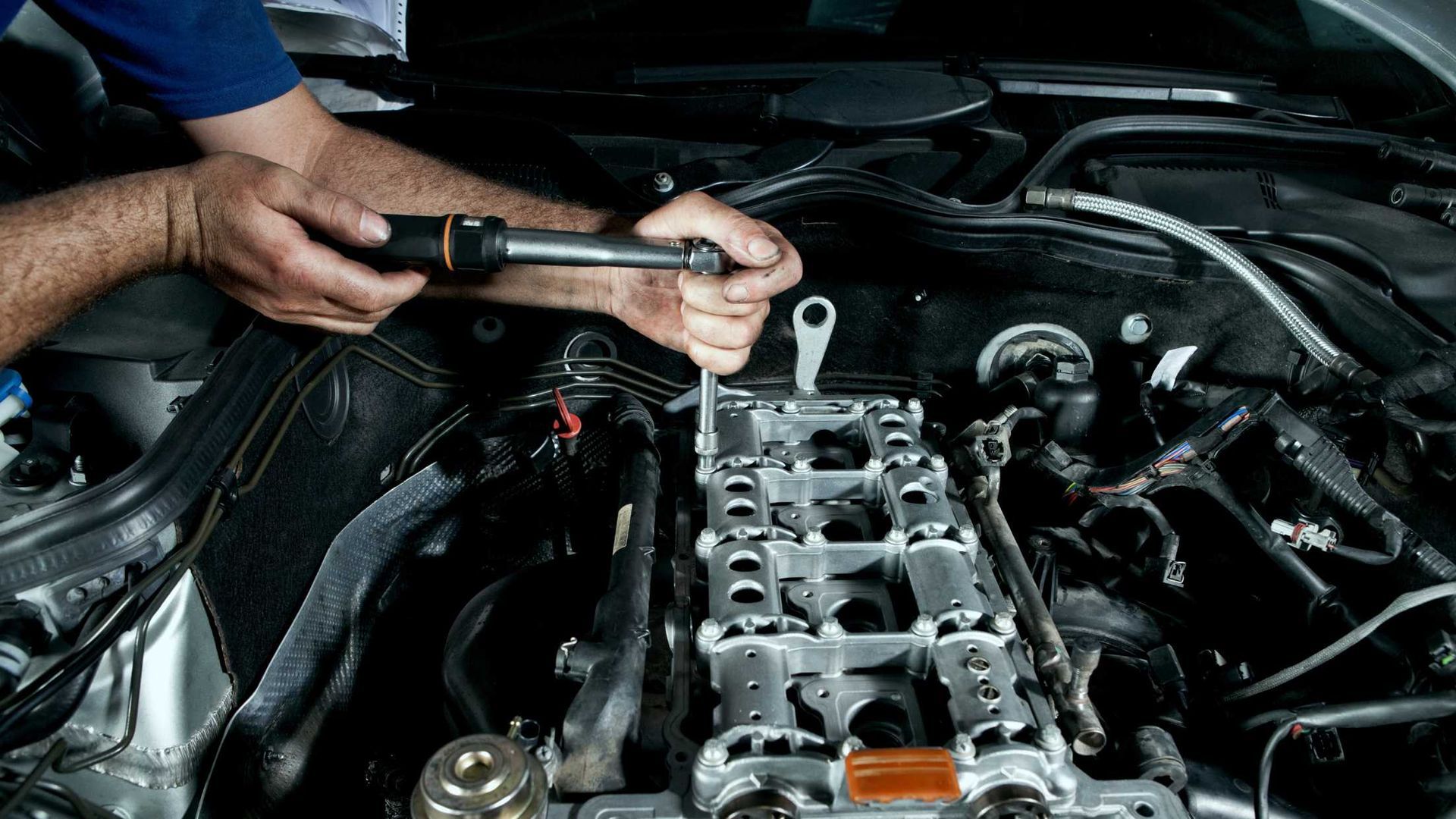 Mechanic tightening bolts on an exposed engine in a car engine bay with a torque wrench