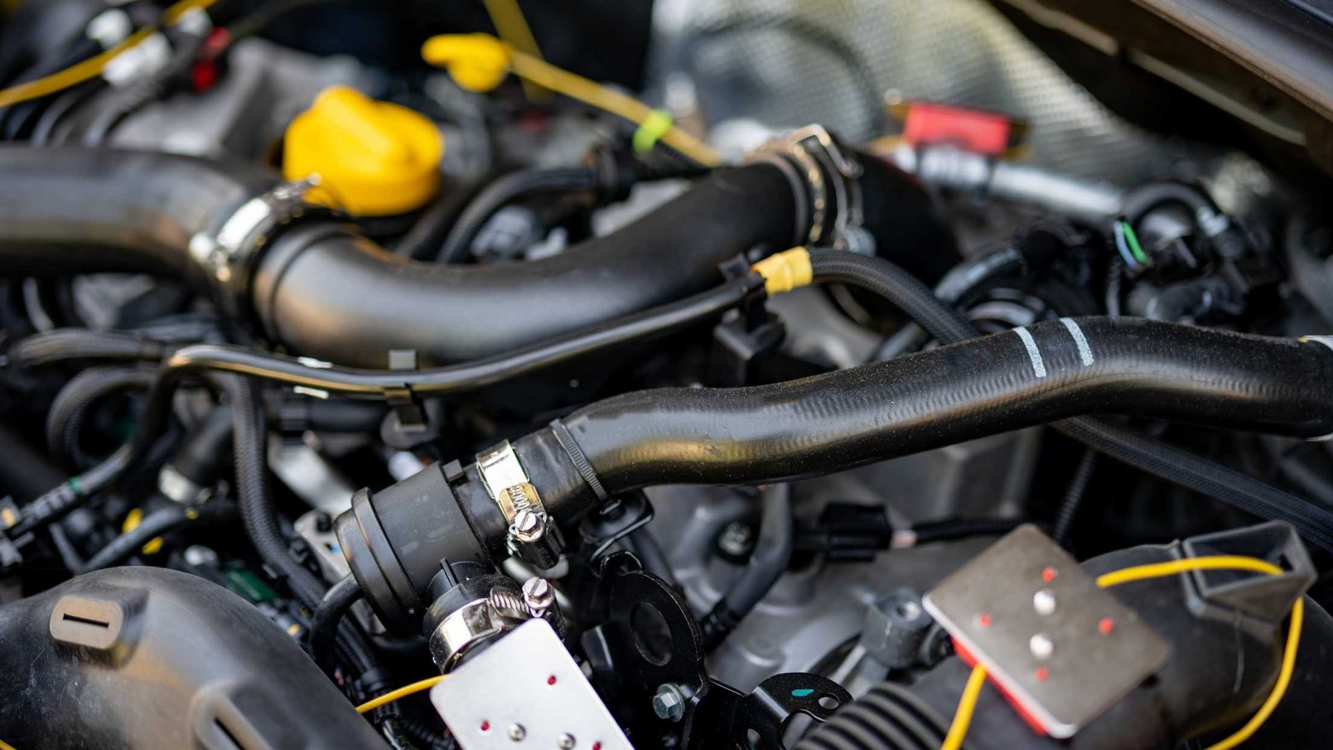 Close-up of an engine bay with black hoses, yellow caps, and wiring in a car.