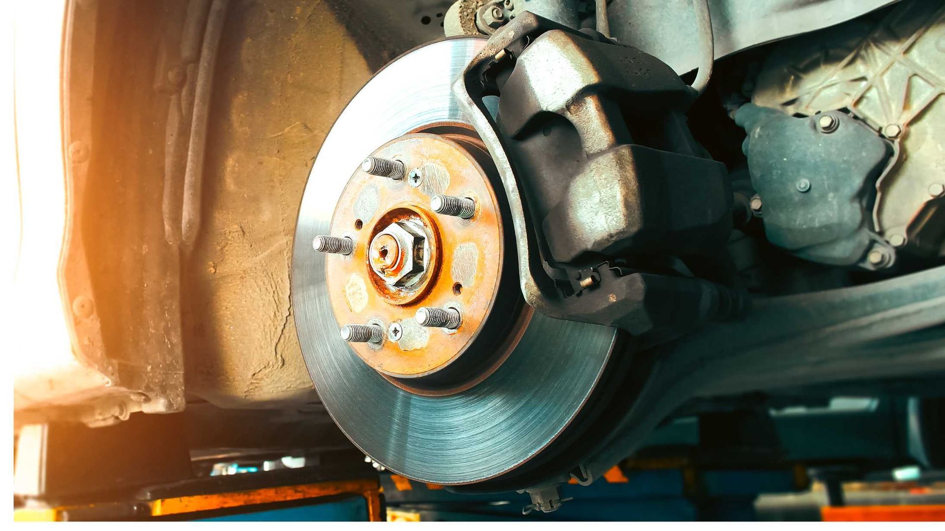 Close-up of a car brake disc and caliper with the wheel removed, showing rust and wear