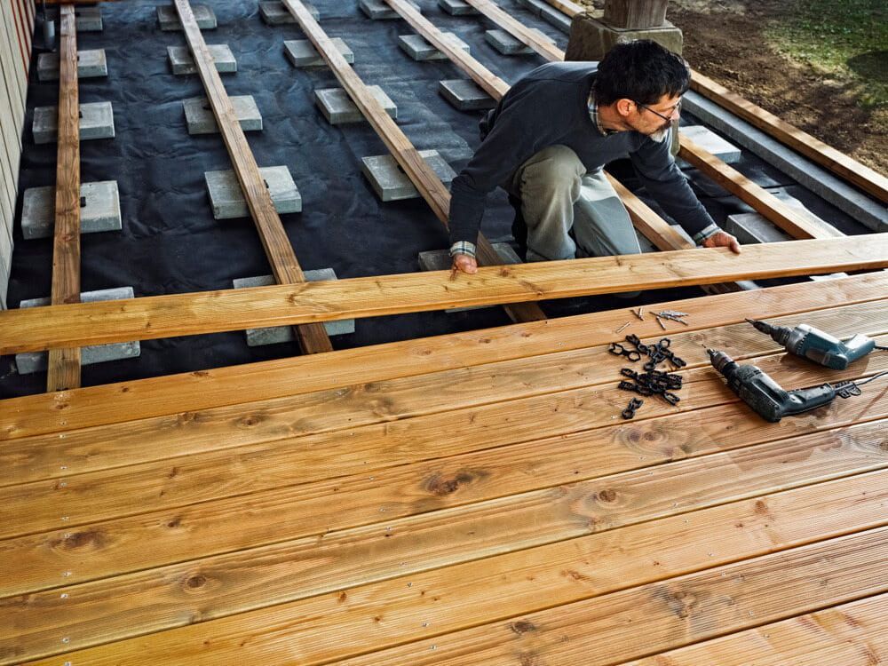A Man Is Working On A Wooden Deck With A Drill — Hitek Frame & Truss In Dubbo, NSW