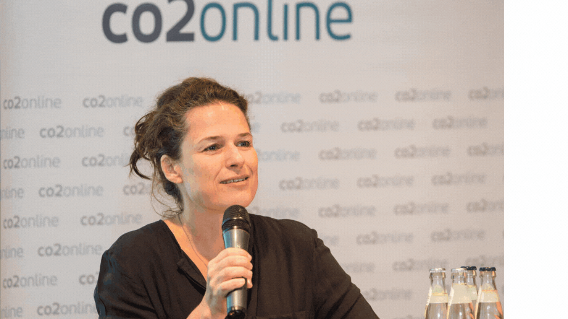 Eine Frau spricht bei einer co2online-Veranstaltung in ein Mikrofon; verschiedene Infografiken werden eingeblendet