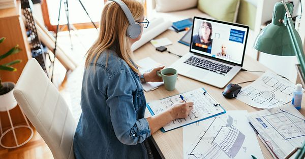 Eine Person arbeitet während eines Webinars an einem Schreibtisch mit Laptop, umgeben von Papieren und einer Kaffeetasse.
