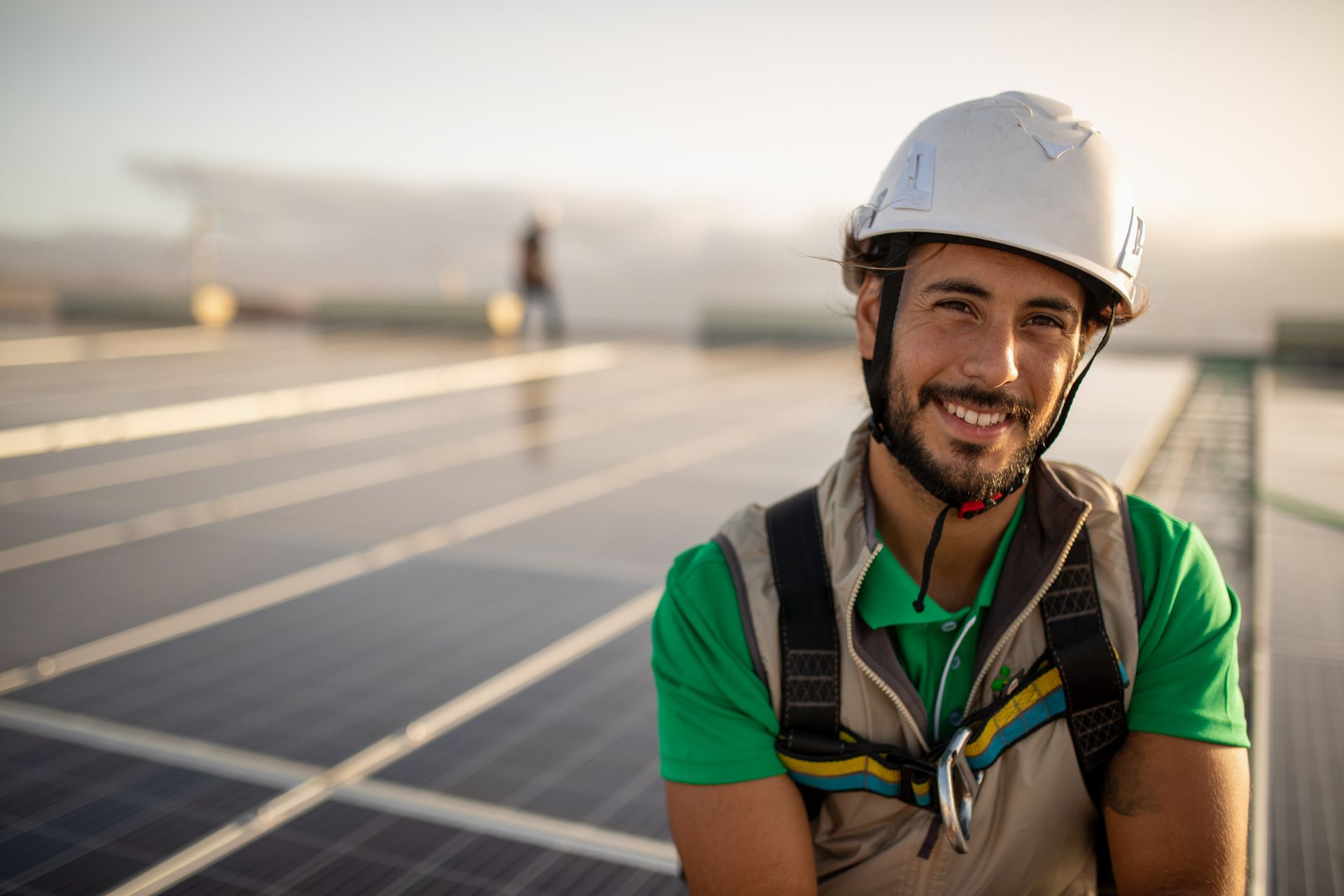Arbeiter mit Schutzhelm und Sicherheitsweste lächelt bei Sonnenuntergang auf einer Solaranlagenbaustelle
