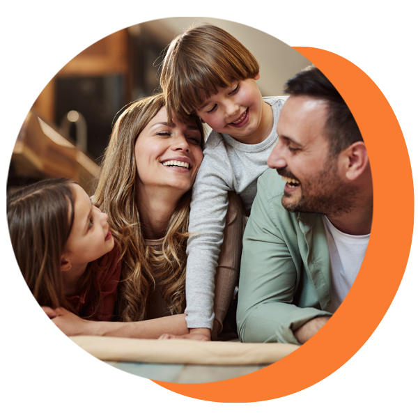 Family of four laughing, leaning together, with natural smiles, warm tones, in a home setting.