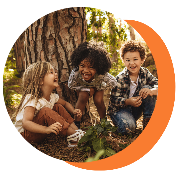 Three children are sitting under a tree in the woods.