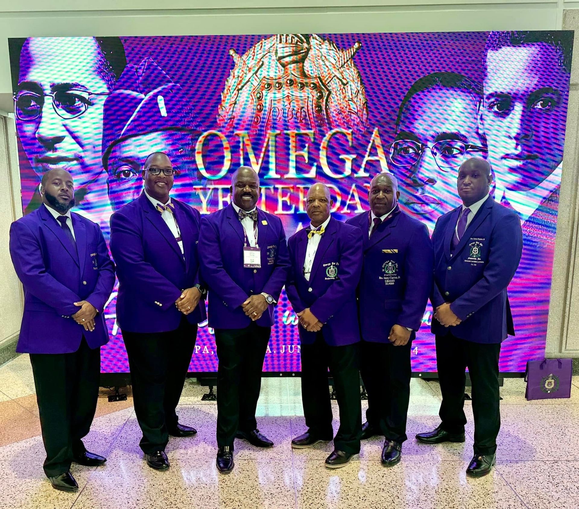 Men in purple blazers stand before a 