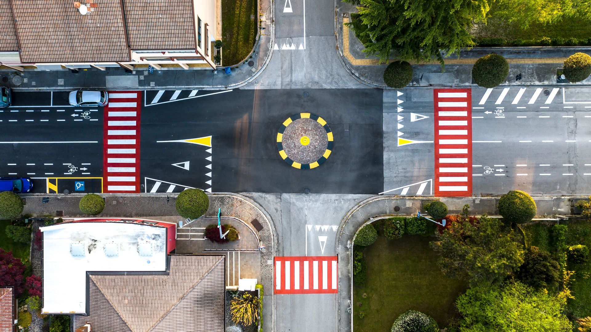 Vista dall'alto di un incrocio stradale con una piccola rotonda centrale e attraversamenti pedonali.