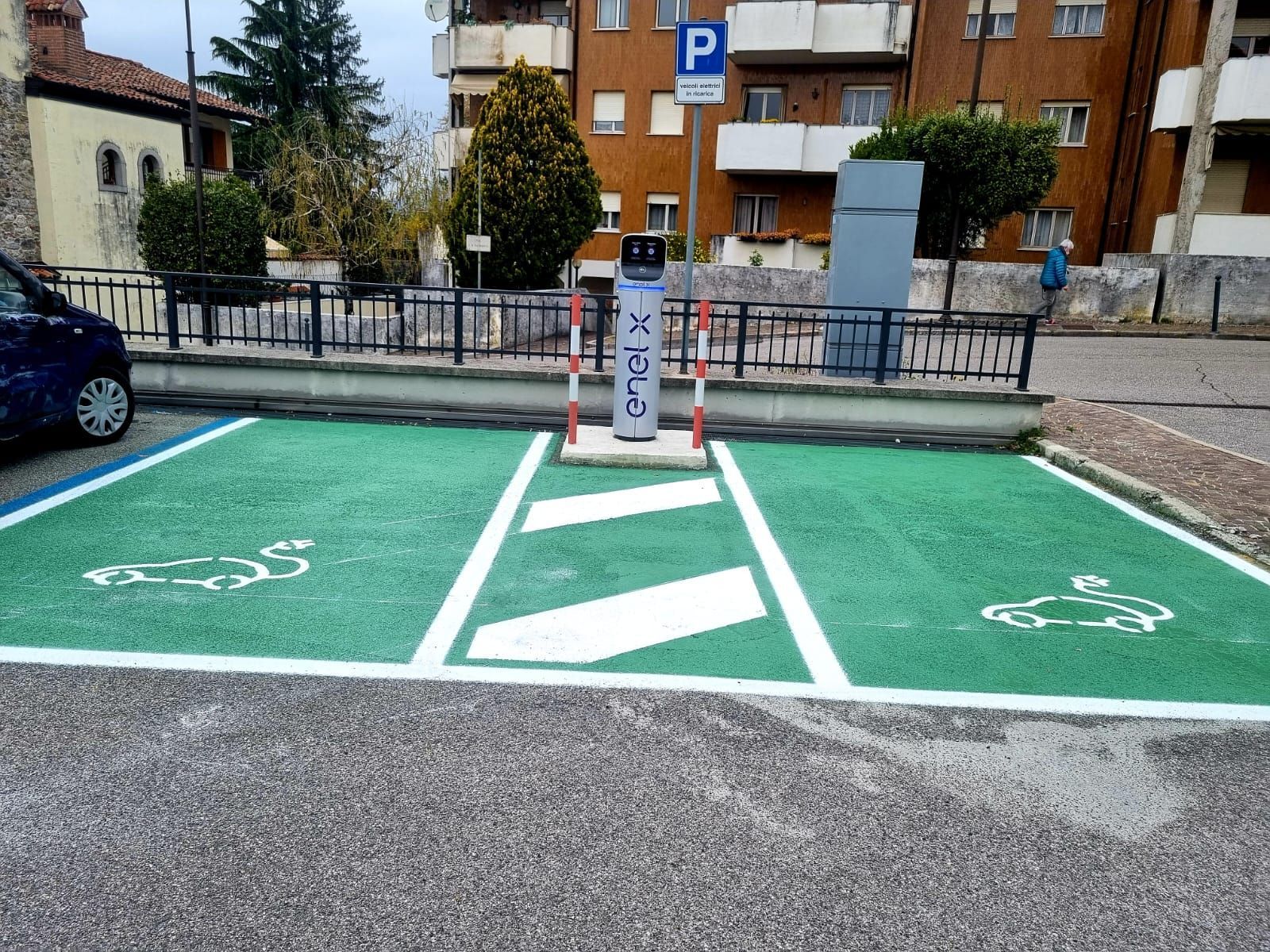 Stazione di ricarica per veicoli elettrici nel parcheggio, dipinta di verde, con simboli di auto, colonnina di ricarica.
