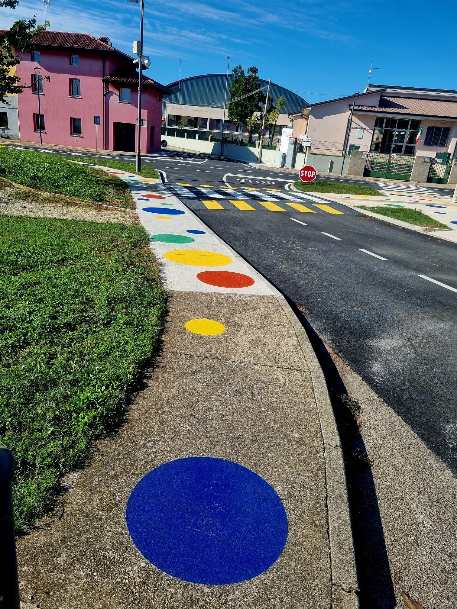 Marciapiede con cerchi colorati che conduce alle strisce pedonali.