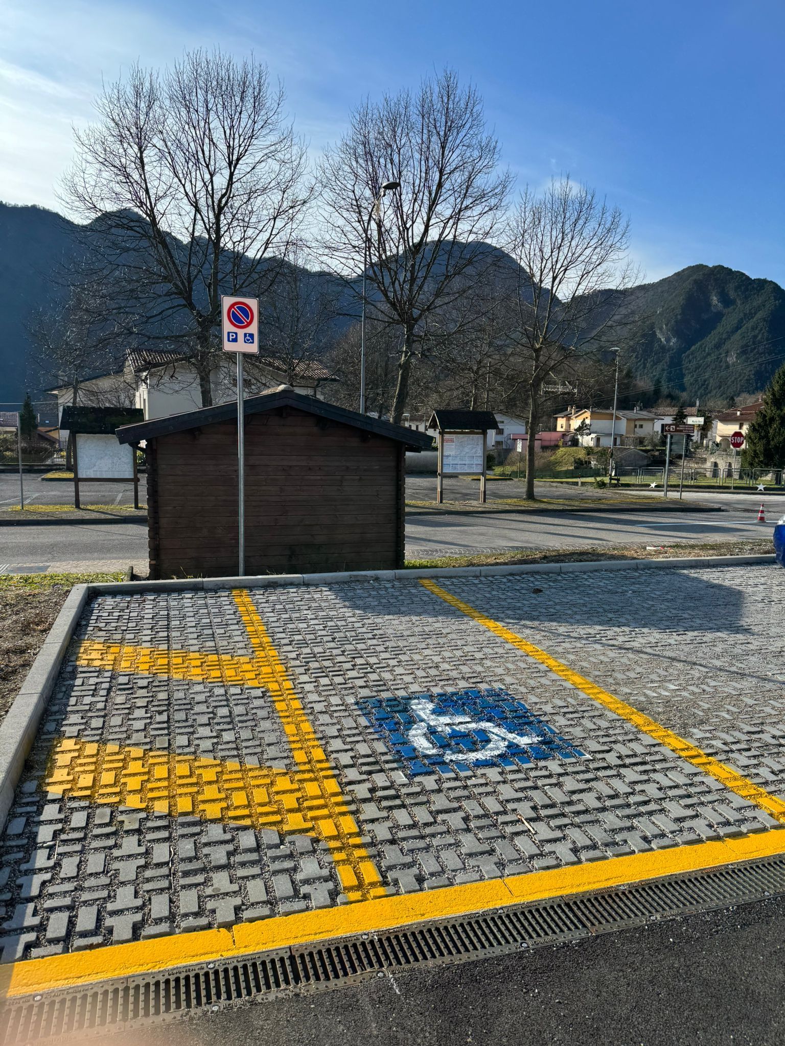 Posto auto per disabili in un parcheggio, contrassegnato da un simbolo blu e linee gialle, con montagne sullo sfondo.
