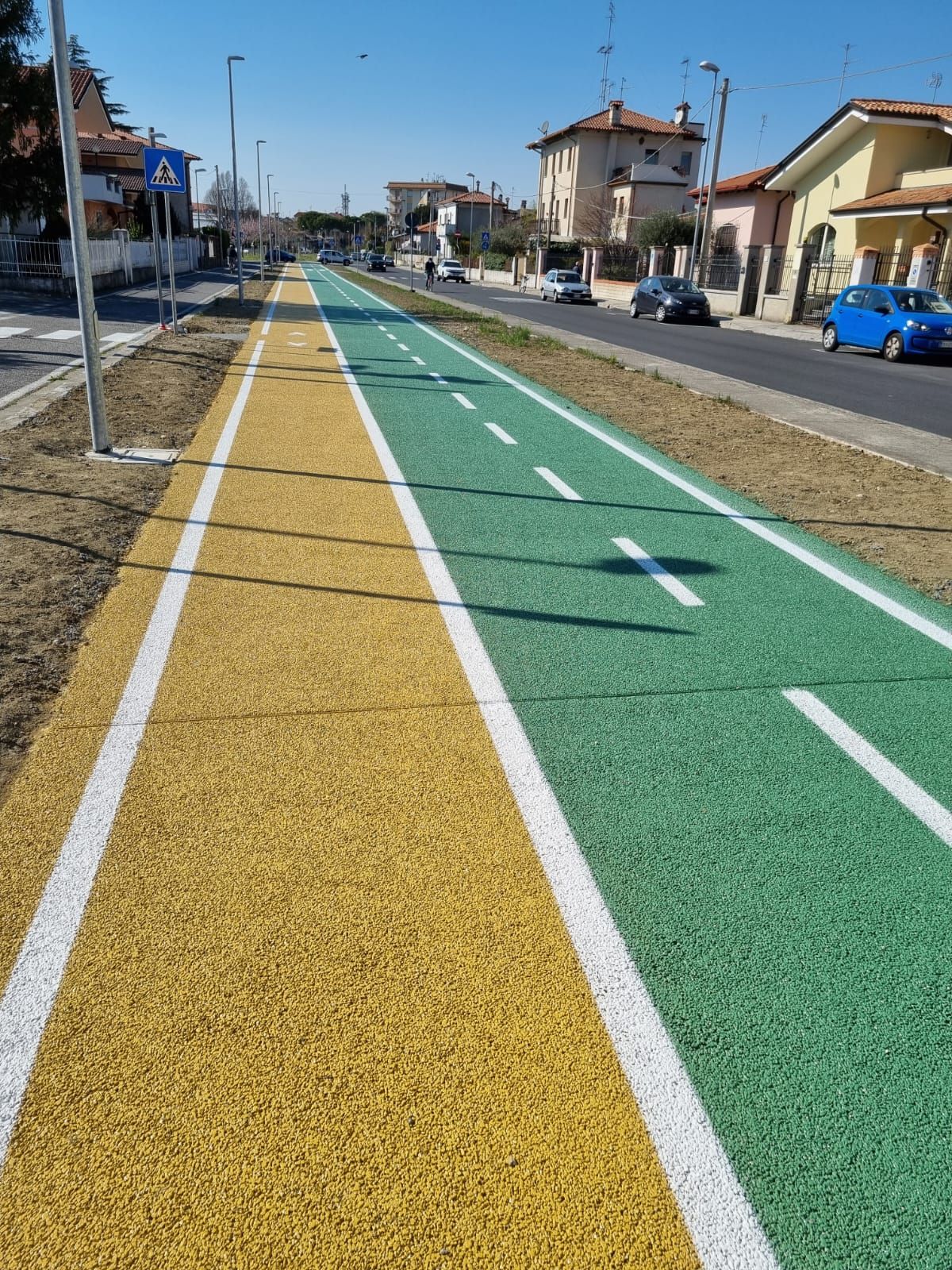Pista ciclabile con superfici verdi e gialle, linee bianche.