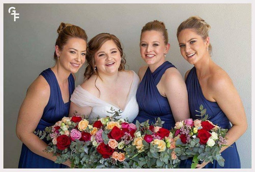 A Bride and Her Bridesmaids Are Posing for a Picture While Holding Bouquets of Flowers — Just Formals in Winnellie, NT