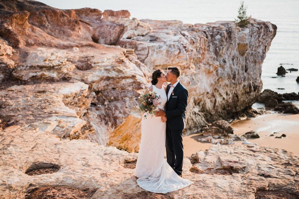 A Bride and Groom Are Kissing on Top of a Rocky Cliff Near the Ocean — Just Formals in Winnellie, NT