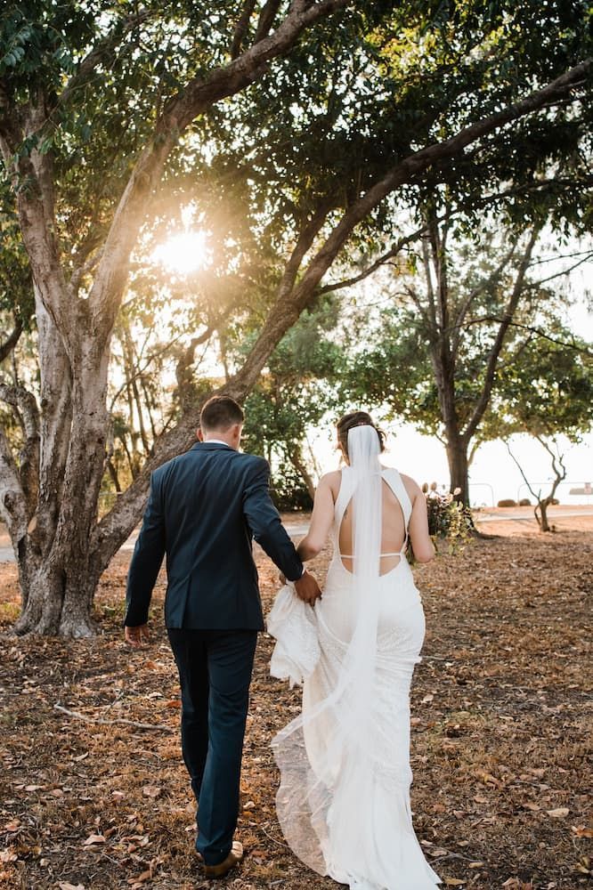 A Bride and Groom Are Walking Through a Forest Holding Hands — Just Formals in Winnellie, NT